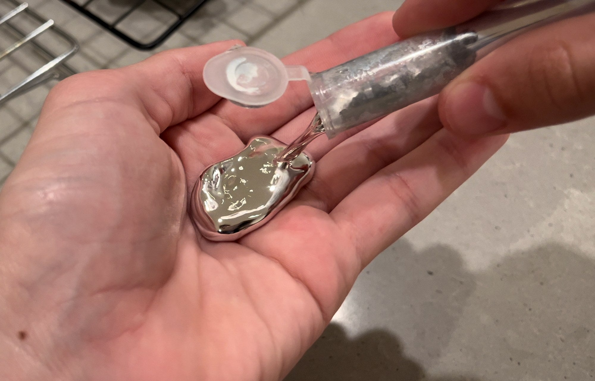 Liquid gallium being poured from a vial into an open palm, where it pools as a bright silver droplet